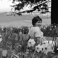 Unidentified student in daffodil patch outside the Cowell College dining hall, with the housing trailers in the background